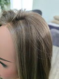 A close-up side view of a mannequin head wearing a long, straight wig with highlighted brown and blonde tones.