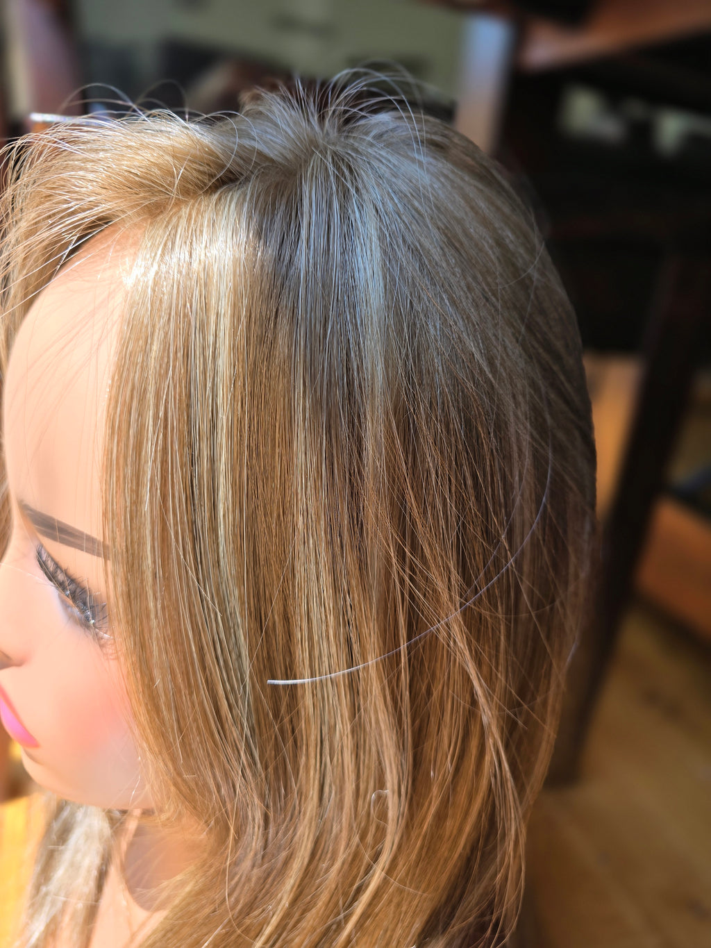 Close-up side view of a mannequin or wig display head with long, straight, highlighted hair in warm blonde and light brown tones.