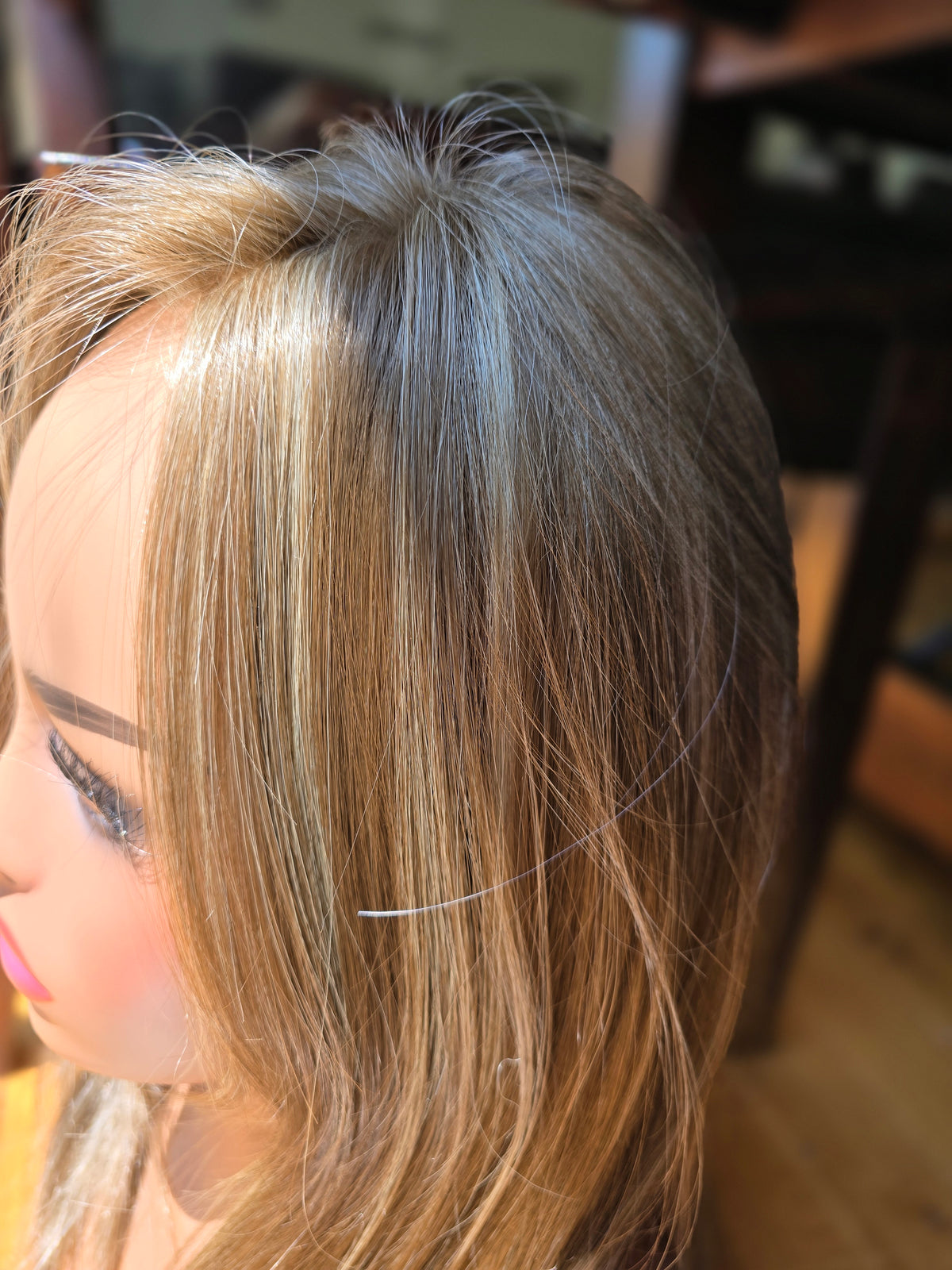 Close-up side view of a mannequin or wig display head with long, straight, highlighted hair in warm blonde and light brown tones.